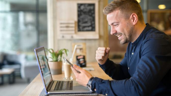 Autonomo-en-Andorra Hombre joven sonriente trabajando como autónomo desde un portátil en un café moderno, tramitando su residencia en Andorra